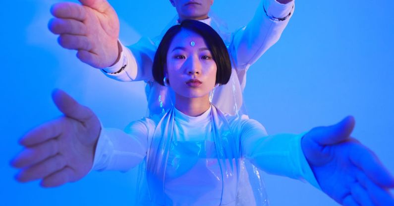 Collaborative Robots - Young Man and Woman in Futuristic Outfits Standing in Studio with Blue Lighting and Holding Their Arms Up
